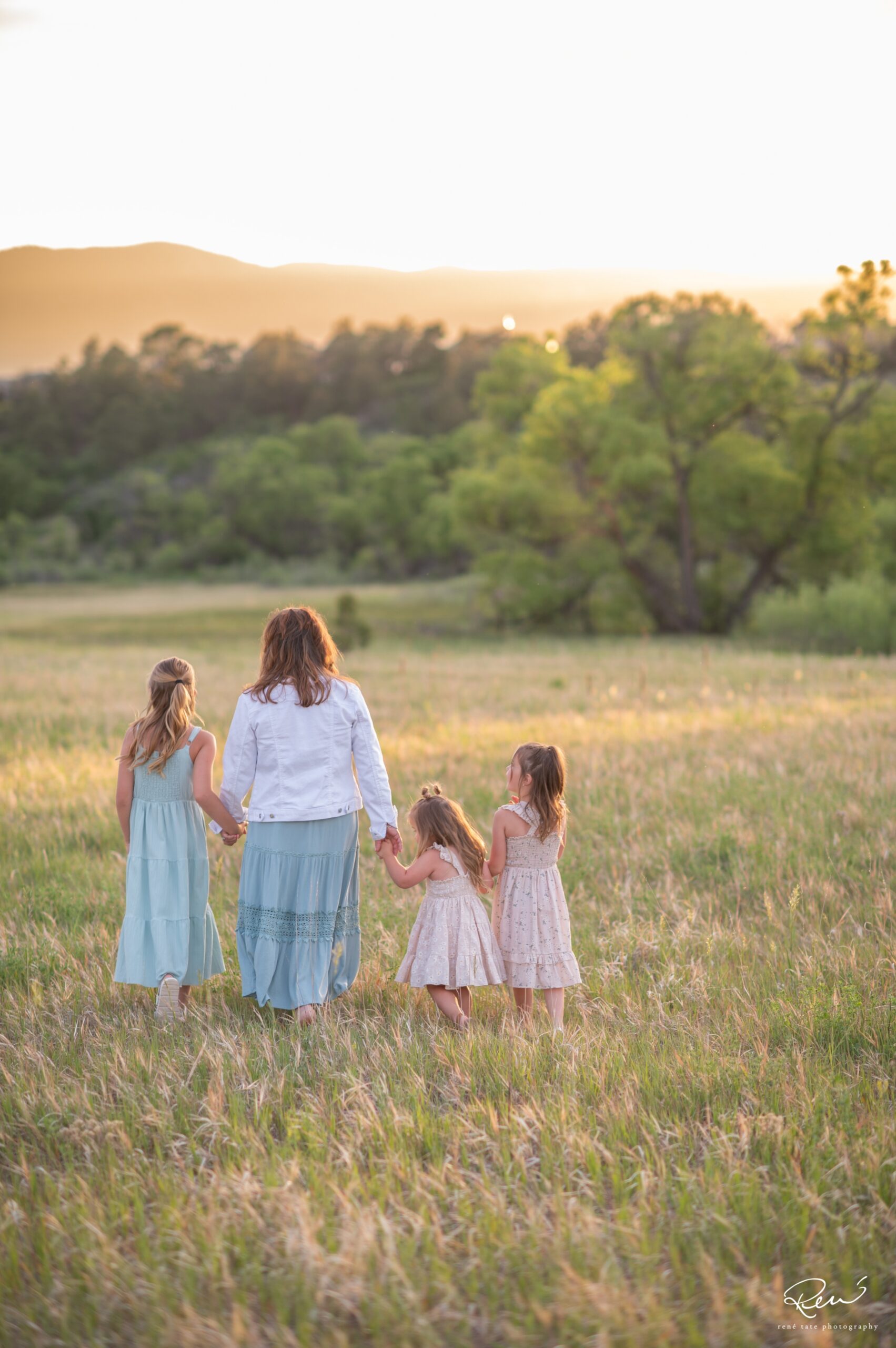 Grandmother walking through field at sunset her granddaughters  during a golden hour family photo session in Colorado Springs.