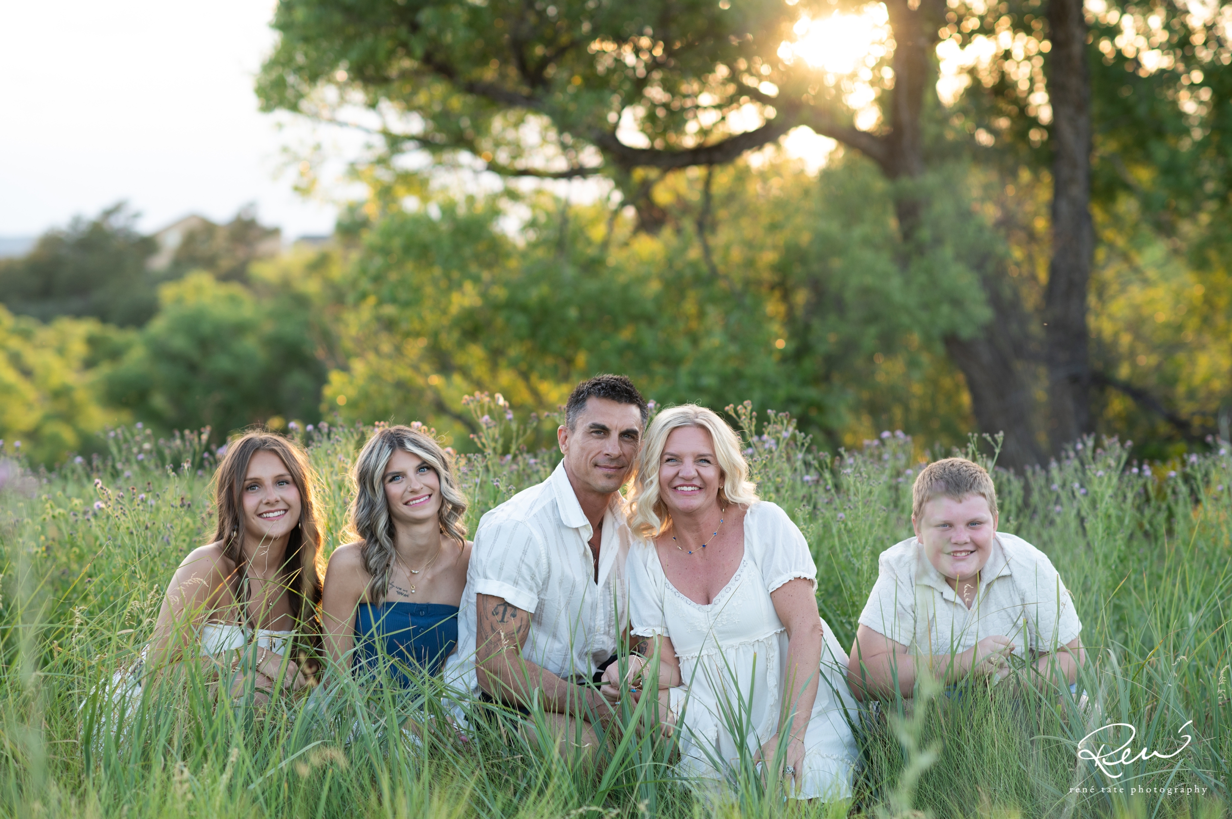 a family of five stand together in an open field of golden grass with their family dog and mountains in the background in Colorado Springs CO